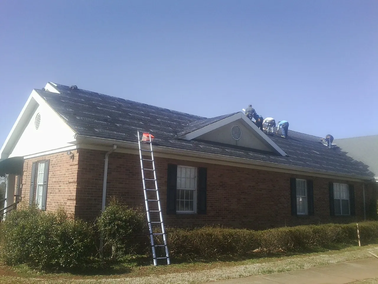 Crew tearing shingles off a brick ranch roof with a ladder set — Emergency Roof Repair work by our crew in Wheatland